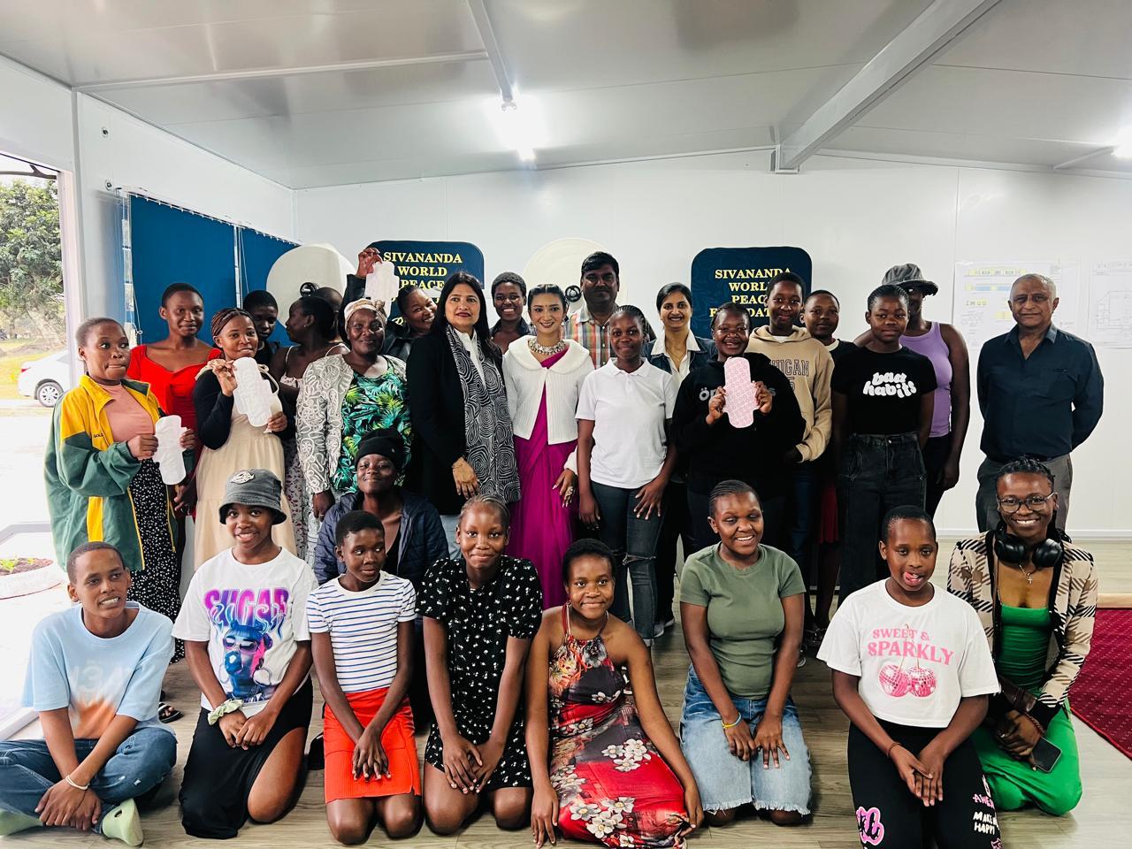 A large group of women and girls at a community menstrual health session, several holding sanitary pads