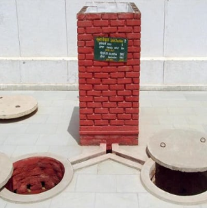 Two circular pit covers set into a paved floor on either side of a small brick inspection pillar carrying a painted sign